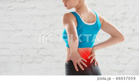 Cropped view of young woman feeling pain in her lower back after workout at gym, copy space Cropped view of young woman feeling pain in her lower back after workout at gym, copy space 66037059