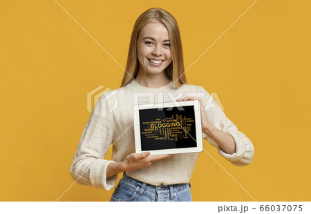 Smiling blonde girl showing tablet computer with modern blogging terms on screen, orange background. Collage 66037075