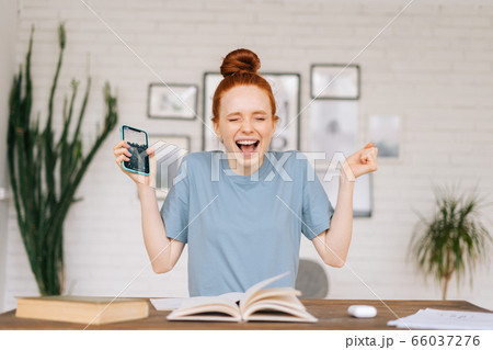 Happy redhead young woman is feeling euphoric reading good amazing news on cell phone 66037276