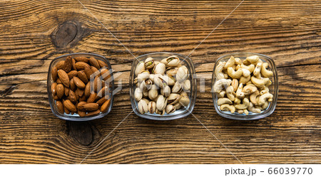 Almond, pistachio and cashew in a small plates which standing on a wooden vintage table. Nuts is a healthy vegetarian protein and nutritious food. Nuts on rustic old wood. Almond, pistachio and cashew in a small plates which standing on a wooden vintage table. Nuts is a healthy vegetarian protein and nutritious food. Nuts on rustic old wood. 66039770
