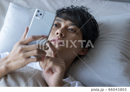 ベッドに寝ながらスマートフォンを見る若い男性 ベッドに寝ながらスマートフォンを見る若い男性 66043803