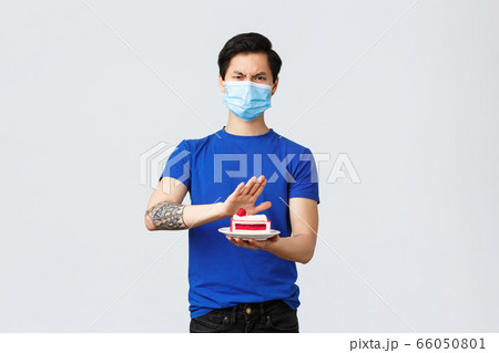 Self-quarantine, home lifestyle and celebration concept. Angry disgusted young asian guy dont like dessert, rejecting awful disgusting cake, frowning disappointed, wear medical mask Self-quarantine, home lifestyle and celebration concept. Angry disgusted young asian guy dont like dessert, rejecting awful disgusting cake, frowning disappointed, wear medical mask 66050801
