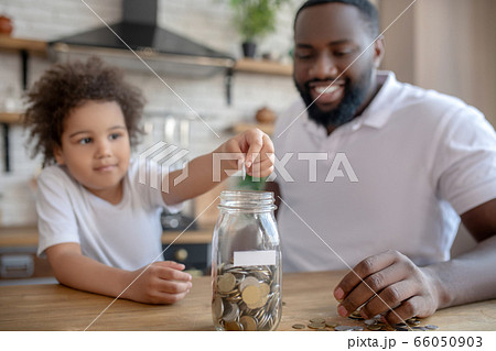 Cute curly-haired kid putting coins into the moneybank Cute curly-haired kid putting coins into the moneybank 66050903