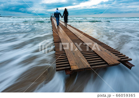 Two people go down the wooden sea pier into the 66059365