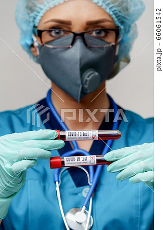 medical doctor nurse woman wearing protective mask and gloves - holding negative and positive coronavirus COVID-19 blood test 66061542