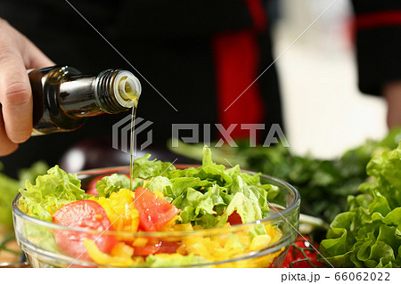 Young chef pouring down olive oil into salad Young chef pouring down olive oil into salad 66062022