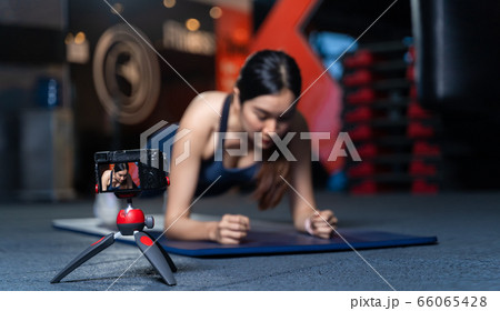 The camera on the tripod is taking pictures or videos. Asian Women Trainer In Good Shape Teaching or performing a sample of plank poses is a bodyweight exercise in online training concept 66065428