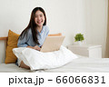 Cute young woman work at home on laptop computer while sitting on bed,looking at camera and brightly smile. 66066831