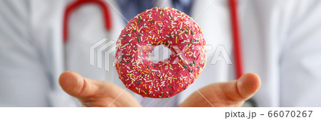 Doctor in office holding in hand pink doughnut Doctor in office holding in hand pink doughnut 66070267