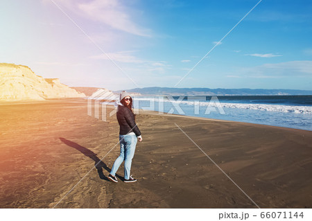 Woman in a hat walking on Pacific ocean coast on windy day 66071144