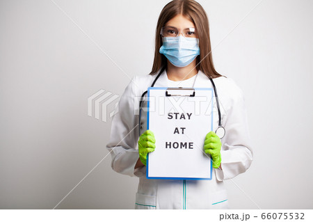 Woman in mask holding blank with inscription stay at home calling for stop spreading covid-19. 66075532