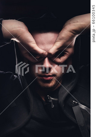 A low key portrait of a man in a hooded hand gesture makes a sperm hero mask. The concept of anonymity and privacy 66100345