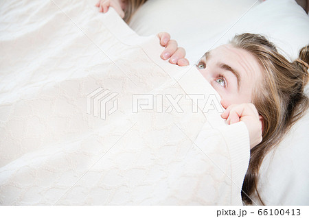 A young attractive man peeks out from under the blankets hiding behind them with fear when he wakes up. The concept of male fears related to sleep and intimate life in the family 66100413