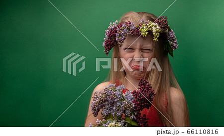 Overjoyed, a young woman, incomparable in a lilac wreath with a European face with a bunch, falls in love with a green background with bright daylight. Grimace 66110816