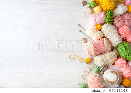 Woolen and cotton bright yarn lies in a basket. Glasses lie on a white wooden background. Woolen and cotton bright yarn lies in a basket. Glasses lie on a white wooden background. 66111148