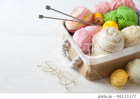 Woolen and cotton bright yarn lies in a basket. Glasses lie on a white wooden background. 66111177