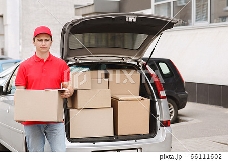 Express delivery to home. Courier holds box near open car with parcels 66111602