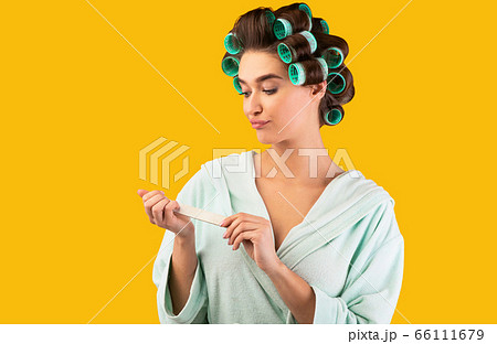 Displeased Housewife Doing Manicure With Nail Buffer On Yellow Background Displeased Housewife Doing Manicure With Nail Buffer On Yellow Background 66111679
