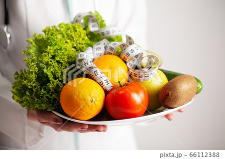 Diet concept, nutritionist holding a full plate of fresh fruit with measuring tape Diet concept, nutritionist holding a full plate of fresh fruit with measuring tape 66112388