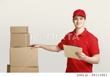 Parcel control by post worker. Smiling courier in uniform holds tablet for notes and puts his hand on cardboard box Parcel control by post worker. Smiling courier in uniform holds tablet for notes and puts his hand on cardboard box 66112661