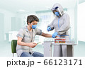 フェイスシールドをして防護服を着た医療従事者が陽性患者に投薬のワクチン注射をうつ 66123171