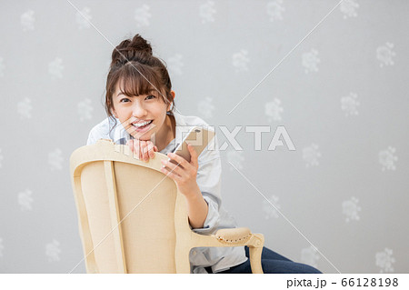 クラシックチェアに座りスマホを眺める女性（カメラ目線） 66128198