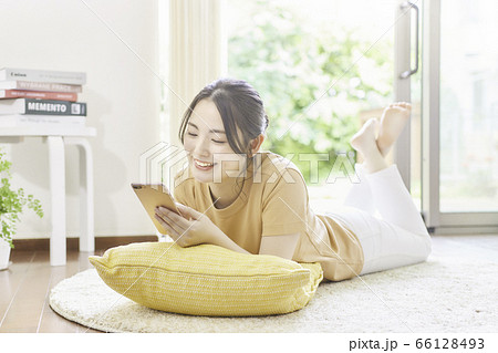 リビングで寝そべってスマホを使う若い女性 洋書は著作権フリーのものを使用 の写真素材