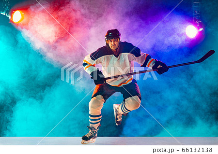 Male hockey player with the stick on ice court and dark neon colored background 66132138