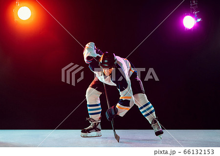 Male hockey player with the stick on ice court and dark neon colored background 66132153