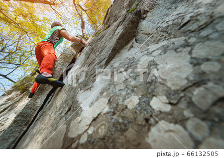 A man is training in free climbing on a rock stone in the forest on a sunny day. The concept of leisure activities of an active lifestyle of people aged 66132505