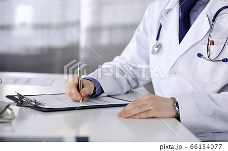 Unknown male doctor sitting and working with clipboard of medication history record in clinic at his working place, close-up. Young physician at work. Perfect medical service, medicine concept 66134077