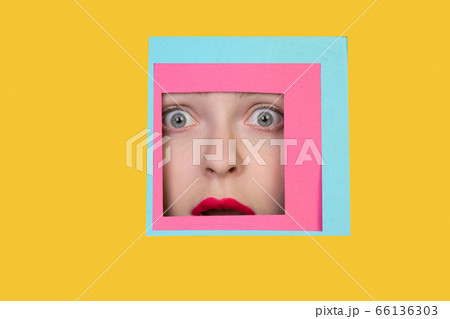 Face of caucasian woman peeking throught square in yellow background 66136303