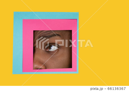 Eye of african-american man peeking throught square in yellow background Eye of african-american man peeking throught square in yellow background 66136367