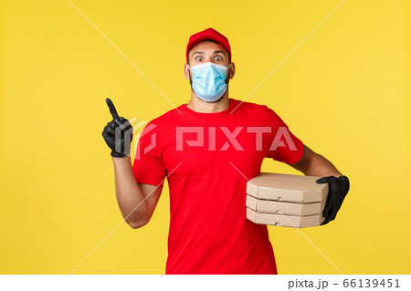 Food delivery, tracking orders, covid-19 and self-quarantine concept. Shocked young courier in red uniform and medical mask, pointing finger upper left corner as deliver pizza to clients house Food delivery, tracking orders, covid-19 and self-quarantine concept. Shocked young courier in red uniform and medical mask, pointing finger upper left corner as deliver pizza to clients house 66139451