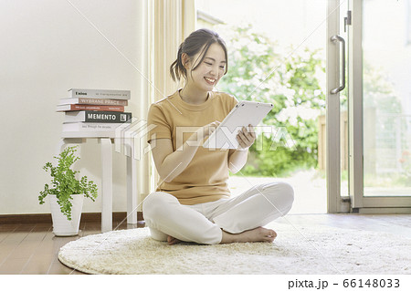 リビングでラグマットの上に座ってタブレットを使う若い女性 洋書は著作権フリーのものを使用 の写真素材