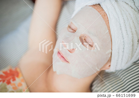 Young red-haired woman relaxing on a bed. Sheet mask on her face Young red-haired woman relaxing on a bed. Sheet mask on her face 66151699