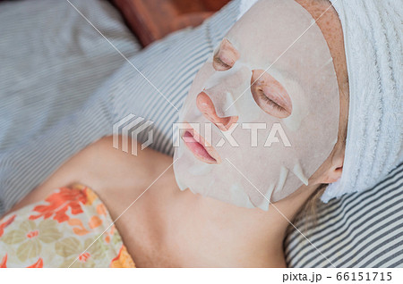 Young red-haired woman relaxing on a bed. Sheet mask on her face Young red-haired woman relaxing on a bed. Sheet mask on her face 66151715