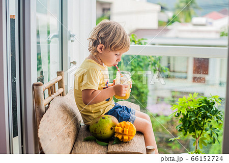 Boy drinking juicy smoothie from mango in glass mason jar with striped red straw on old wooden background. Healthy life concept, copy space 66152724