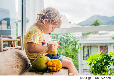 Boy drinking juicy smoothie from mango in glass mason jar with striped red straw on old wooden background. Healthy life concept, copy space 66152726