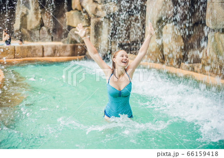 Young woman relaxing under a waterfall in aquapark Young woman relaxing under a waterfall in aquapark 66159418