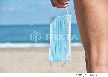 man with a surgical mask in his hand on the beach 66170658