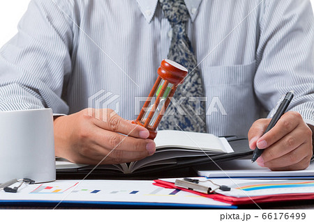 businessman taking note from the sale figure report and checking time from sandglass by close up businessman taking note from the sale figure report and checking time from sandglass by close up 66176499