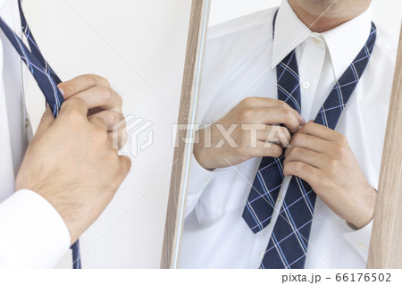 鏡を見ながらネクタイを締める、ワイシャツを着た男性 66176502