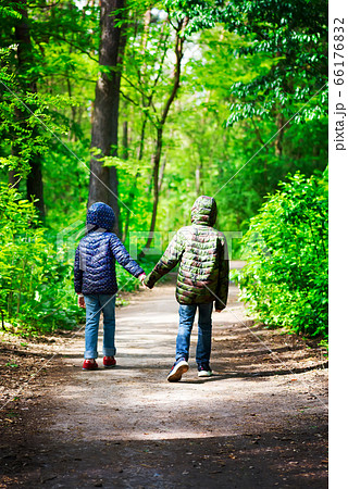 Two children in jackets are walking around city park or forest on a safe distance in a sunny day holding hands Two children in jackets are walking around city park or forest on a safe distance in a sunny day holding hands 66176832
