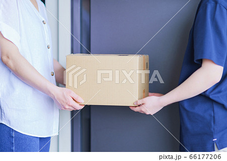 ネット通販の配達小包を届ける配達員とマンションの玄関先で受け取る主婦 66177206