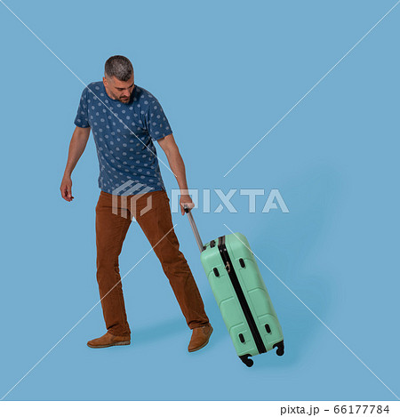 Man carries plastic suitcase holding it by folding handle. Cut out on blue background. Handsome Caucasian man goes on business trip. Vacation concept 66177784