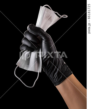 Hand in black gloves holding disposable face mask isolated on black background Hand in black gloves holding disposable face mask isolated on black background 66181725
