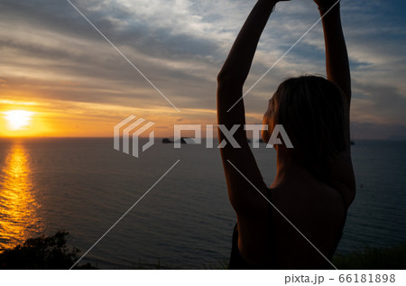 Silhouette of a woman watches sunset over a sea or ocean on a tropical island. Silhouette of a woman watches sunset over a sea or ocean on a tropical island. 66181898