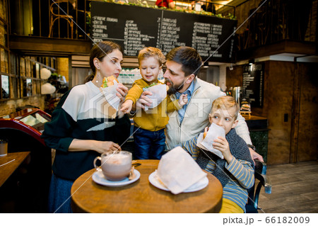 Family having breakfast at city cafe with blurred interior on the background. Adorable children and their parents eating fresh tasty croissants and drinking cocoa drink or coffee 66182009