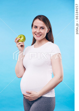 Happy pregnant female with granny smith apple touching bottom of her belly Happy pregnant female with granny smith apple touching bottom of her belly 66184057